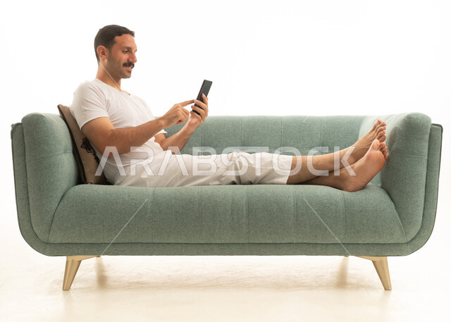 رجل سعودي يستخدم الهاتف الذكي على أريكة خضراء