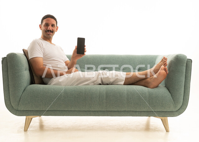 رجل سعودي على أريكة خضراء يمسك بهاتف ذكي ذو شاشة سوداء