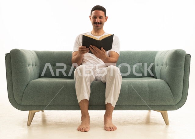 Saudi Man Reading a Book on Teal Sofa
