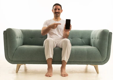 رجل سعودي يشير إلى شاشة هاتف ذكي فارغة على الأريكة