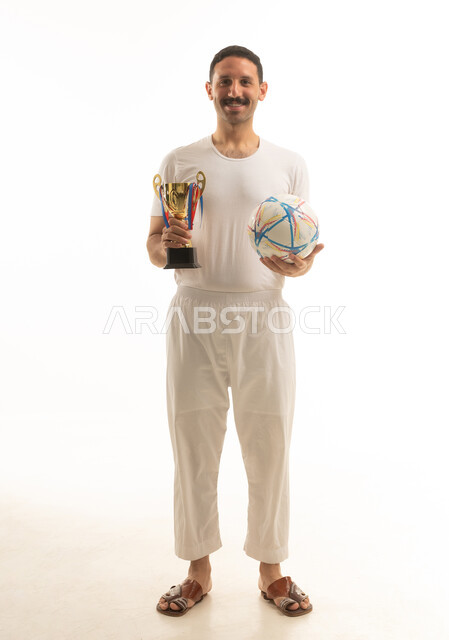 رجل عربي سعودي خليجي يرتدي الفانيلا والسروال يحمل بيده كرة قدم, تشجيع الفريق السعودي, كامل الجسم, خلفيه بيضاء