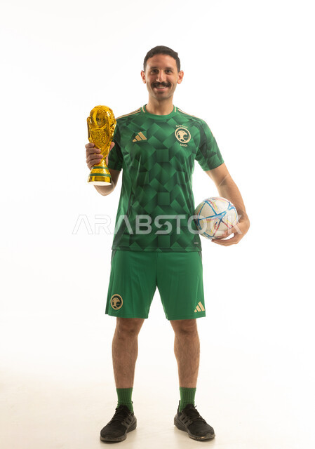 لاعب كرة قدم سعودي يرتدي الزي الرياضي الاخضر يمسك بيده كرة قدم , الفوز بالكأس الذهبي, ايماءات وحركات متنوعه, كامل الجسم, خلفيه بيضاء