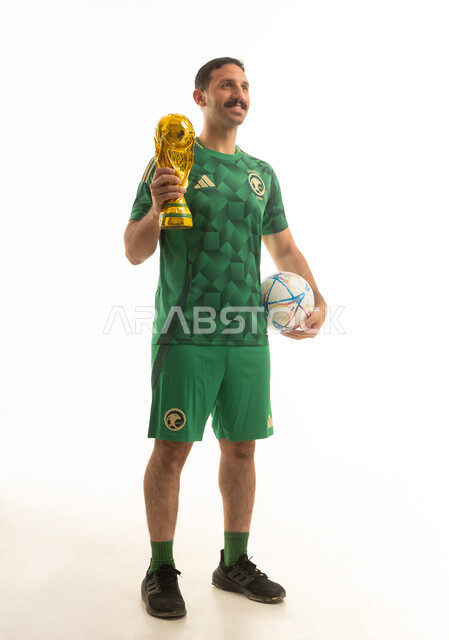 مشجع سعودي بالزي الأخضر يحمل كأس البطولة