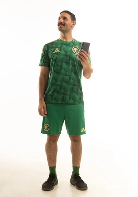 رجل سعودي بزي المنتخب الوطني يحمل هاتفاً ذكياً