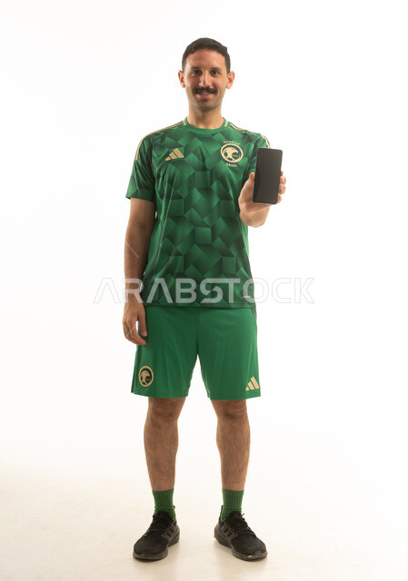 رجل سعودي بزي المنتخب الأخضر يحمل هاتف ذكي خلفية بيضاء