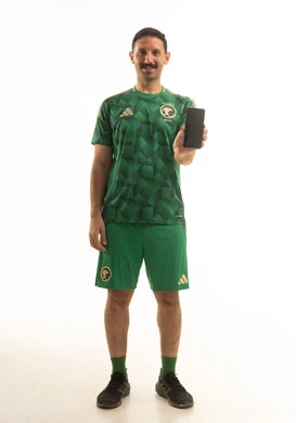 رجل سعودي بزي المنتخب الأخضر يحمل هاتف ذكي خلفية بيضاء