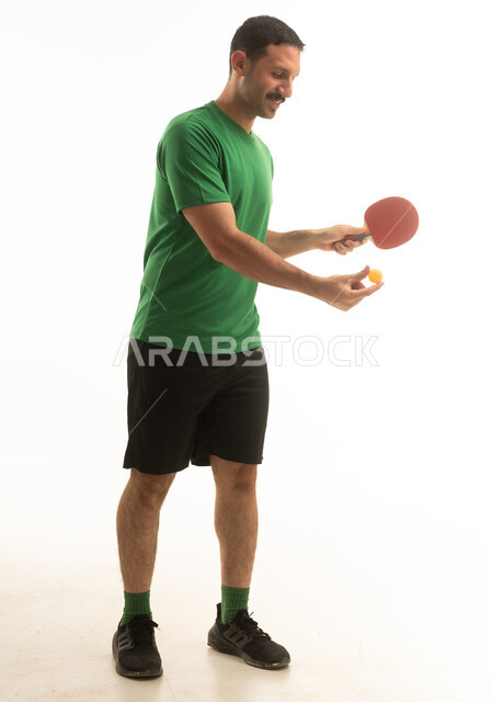 رجل عربي سعودي خليجي يرتدي الزي الرياضي  يلعب تنس الطاوله , نشاط بدني ممتع, الجسم بالطول الكامل, خلفيه بيضاء