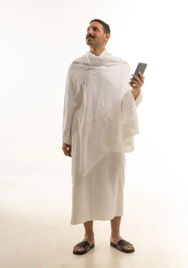بورتريه لرجل عربي سعودي خليجي يرتدي ملابس الاحرام البيضاء ويمسك بيده الهاتف المحمول, اداء مناسك الحج والعمره, العباده والتقرب الى الله, خلفيه بيضاء , الجسم بالطول الكامل