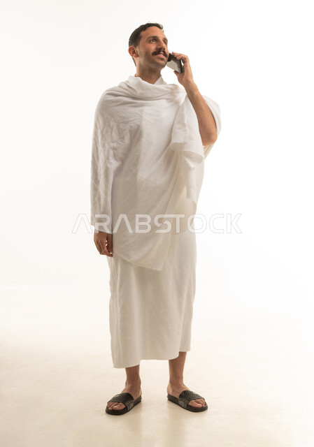 رجل سعودي يرتدي ملابس الإحرام ويستخدم الهاتف المحمول