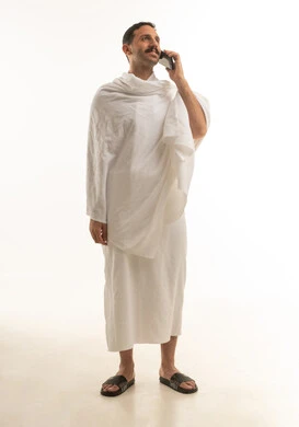 رجل سعودي يرتدي ملابس الإحرام ويستخدم الهاتف المحمول