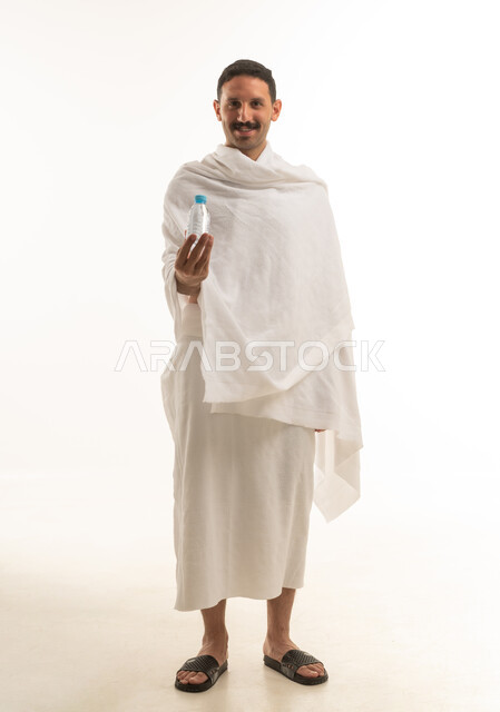 بورتريه لرجل عربي سعودي خليجي يرتدي ملابس الاحرام البيضاء يمسك بيده قارورة ماء , اداء مناسك الحج والعمره, العباده والتقرب الى الله, خلفيه بيضاء , الجسم بالطول الكامل