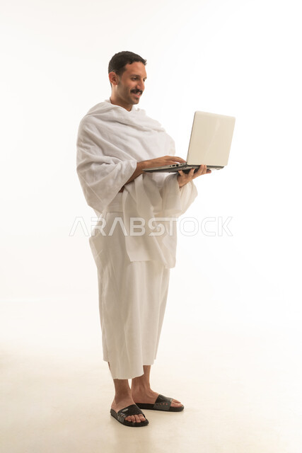 رجل سعودي بملابس الإحرام يحمل لابتوب بخلفية بيضاء