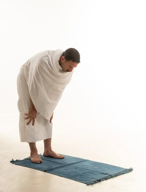 رجل سعودي بملابس الإحرام يؤدي الصلاة خلفية بيضاء