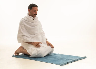 بورتريه لرجل عربي سعودي خليجي يرتدي ملابس الاحرام البيضاء يجلس على سجادة الصلاه ويصلي, اداء مناسك الحج والعمره, العباده والتقرب الى الله, خلفيه بيضاء