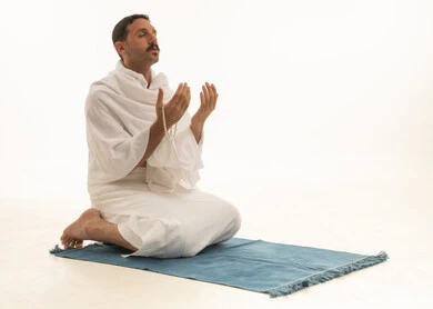 أذكار وأدعية وفرائض، الركوع والسجود والخشوع لله، رجل عربي سعودي خليجي يرتدي بملابس الإحرام يمسك السبحة يجلس على السجادة و يؤدي فريضة الصلاة ، آداء صلاة التراويح فى شهر رمضان الكريم ، الدعاء والتضرع الى الله، خلفية بيضاء