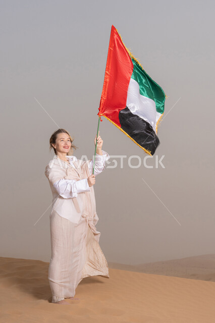Commemorating UAE National Day 1971, the anniversary of the founding of the Union on December 2nd, an Emirati Gulf Arab woman wearing an abaya holds the UAE flag in her hand, standing in the desert. Flag Day, November 3rd, symbolizing love for and pride in the homeland.