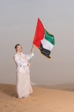ذكرى تأسيس الاتحاد 2 ديسمبر، استذكار اليوم الوطني الاماراتي 1971، إمراة عربية خليجية إماراتية ترتدي العباءة تمسك بيدها علم الإمارات العربية المتحدة تقف في الصحراء، يوم العلم 3 نوفمبر، حب الوطن والاعتزاز به