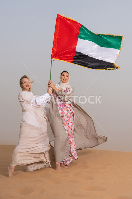 إحياء ذكرى اليوم الوطني الاماراتي 1971، يوم الاتحاد 2 ديسمبر، مفهوم حب الوطن والانتماء إليه، الاحتفال بالأعياد والمناسبات الوطنية، امراتان عربيتان خليجيتان يرتديان العباءة يقفان فى الصحراء يمسكان علم الامارات العربية المتحدة، ذكرى يوم العلم 3 نوفمبر