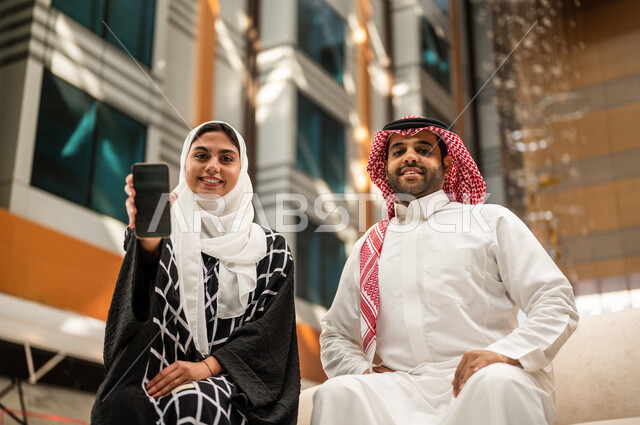 زوجان سعوديان داخل الفندق السياحي ، تمسك المرأة بيدها الهاتف المحمول ، تعرض شاشة سوداء ، إستخدام أجهزة تقنية حديثة، إستخدام وسائل التواصل الإجتماعي ،عرض خدمات وتطبيقات خاصة بالفندق عبر الجوال ، التسويق الإلكتروني ، مفهوم الإعلانات