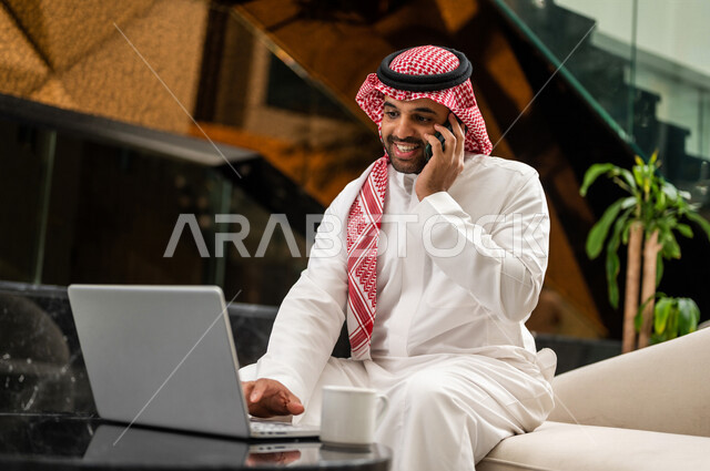 رجل خليجي سعودي بداخل الفنادق السياحية ، يقوم بإجراء مكالمة هاتفية عبر الجوال ، إستخدام جهاز الحاسوب المحمول لإنجاز المهام، إستخدام أجهزة تقنية حديثة، العمل عن بعد ، مهن ووظائف ، جلسة عمل، مفهوم إدارة الأعمال، سياحة وفندقة، التسويق الإلكتروني