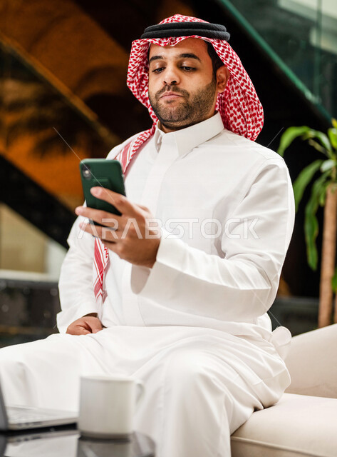 رجل خليجي سعودي بداخل احدى الفنادق السياحية ، يحمل الهاتف المحمول ، إستخدام جهاز الحاسوب المحمول لإنجاز المهام، مفهوم التكنولوجيا وإستخدام أجهزة تقنية حديثة، العمل عن بعد ، مهن و وظائف ، جلسة عمل، مفهوم إدارة الأعمال، سياحة وفندقة، التسويق الإلكتروني