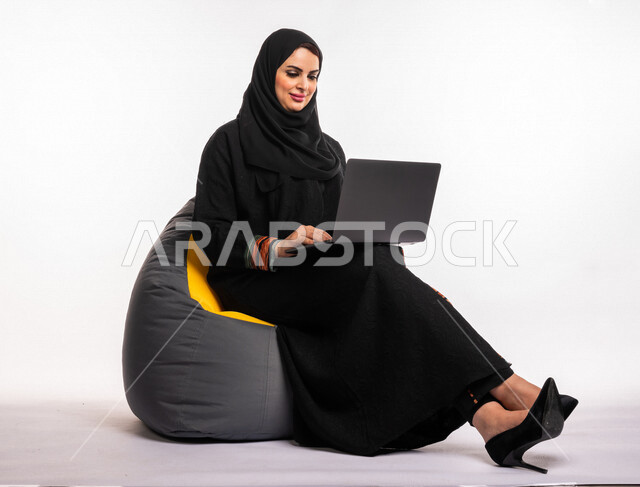  بورتريه لإمرأه عربيه سعوديه خليجيه تجلس على أريكه مريحه, انجاز مهام العمل عبر الحاسوب, إدارة المشاريع عن بعد, اللعب على اللابتوب, إجراء مكالمات فيديو عبر الإنترنت, مشاهدة فلم عبر الجهاز المحمول, تسليه وترفيه, قضاء وقت ممتع