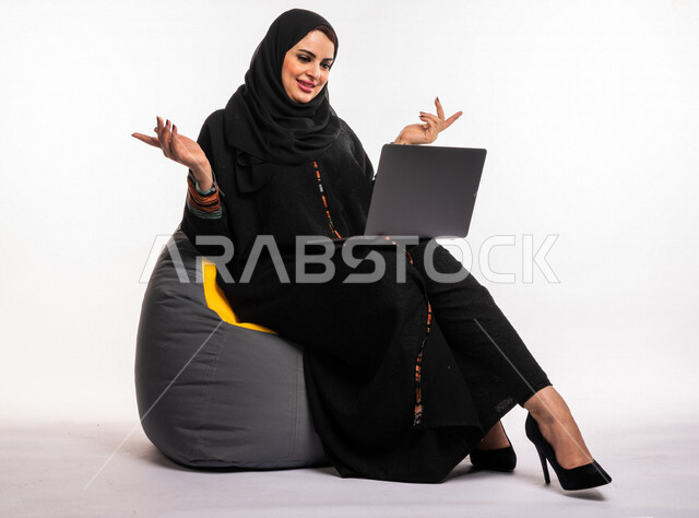  بورتريه لإمرأه عربيه سعوديه خليجيه تجلس على أريكه مريحه, انجاز مهام العمل عبر الحاسوب, إدارة المشاريع عن بعد, اللعب على اللابتوب, إجراء مكالمات فيديو عبر الإنترنت, مشاهدة فلم عبر الجهاز المحمول, تسليه وترفيه, قضاء وقت ممتع