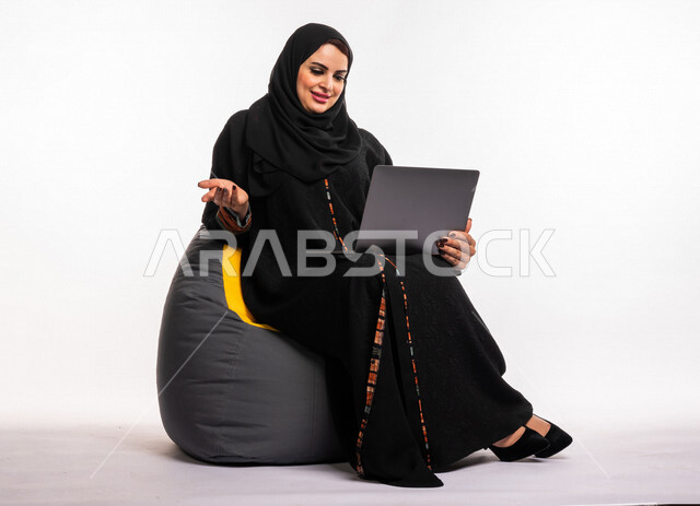  بورتريه لإمرأه عربيه سعوديه خليجيه تجلس على أريكه مريحه, انجاز مهام العمل عبر الحاسوب, إدارة المشاريع عن بعد, اللعب على اللابتوب, إجراء مكالمات فيديو عبر الإنترنت, مشاهدة فلم عبر الجهاز المحمول, تسليه وترفيه, قضاء وقت ممتع