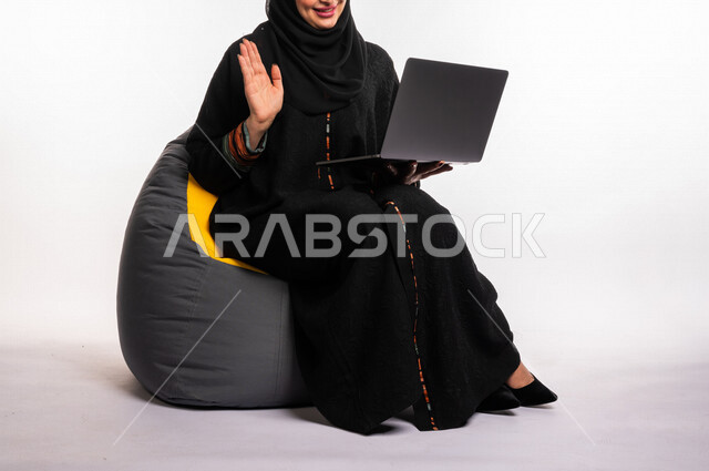 بورتريه لإمرأه عربيه سعوديه خليجيه تجلس على أريكه مريحه, انجاز مهام العمل عبر الحاسوب, إدارة المشاريع عن بعد, اللعب على اللابتوب, إجراء مكالمات فيديو عبر الإنترنت, مشاهدة فلم عبر الجهاز المحمول, تسليه وترفيه, قضاء وقت ممتع