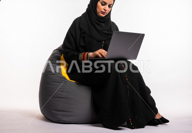  بورتريه لإمرأه عربيه سعوديه خليجيه تجلس على أريكه مريحه, انجاز مهام العمل عبر الحاسوب, إدارة المشاريع عن بعد, اللعب على اللابتوب, إجراء مكالمات فيديو عبر الإنترنت, مشاهدة فلم عبر الجهاز المحمول, تسليه وترفيه, قضاء وقت ممتع