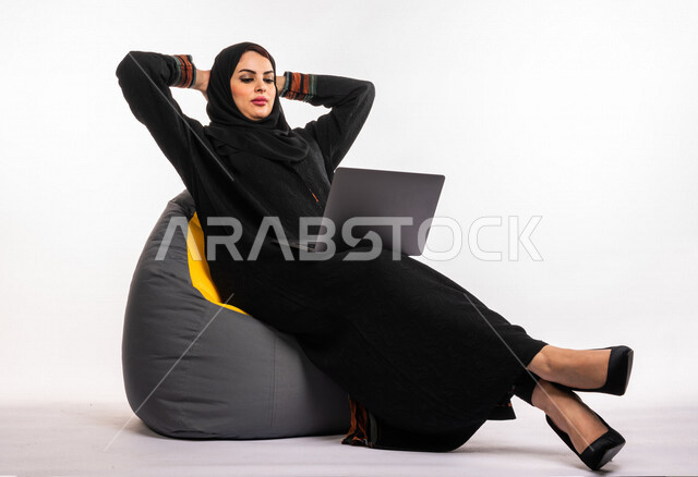  بورتريه لإمرأه عربيه سعوديه خليجيه تجلس على أريكه مريحه, انجاز مهام العمل عبر الحاسوب, إدارة المشاريع عن بعد, اللعب على اللابتوب, إجراء مكالمات فيديو عبر الإنترنت, مشاهدة فلم عبر الجهاز المحمول, تسليه وترفيه, قضاء وقت ممتع