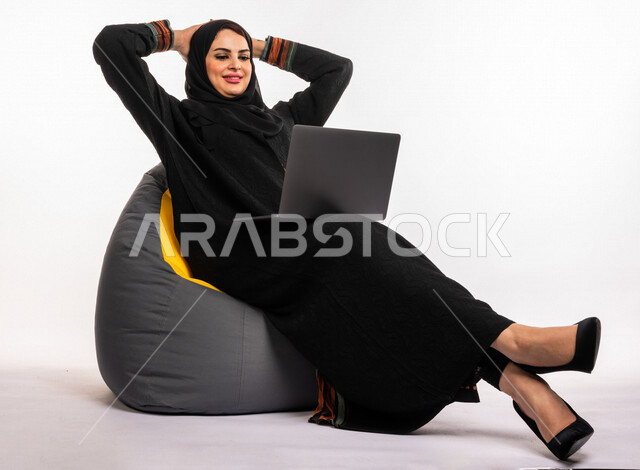 بورتريه لإمرأه عربيه سعوديه خليجيه تجلس على أريكه مريحه, انجاز مهام العمل عبر الحاسوب, إدارة المشاريع عن بعد, اللعب على اللابتوب, إجراء مكالمات فيديو عبر الإنترنت, مشاهدة فلم عبر الجهاز المحمول, تسليه وترفيه, قضاء وقت ممتع