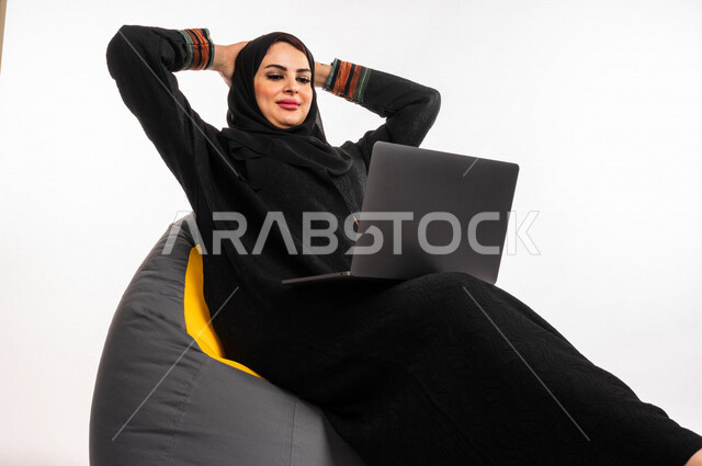  بورتريه لإمرأه عربيه سعوديه خليجيه تجلس على أريكه مريحه, انجاز مهام العمل عبر الحاسوب, إدارة المشاريع عن بعد, اللعب على اللابتوب, إجراء مكالمات فيديو عبر الإنترنت, مشاهدة فلم عبر الجهاز المحمول, تسليه وترفيه, قضاء وقت ممتع