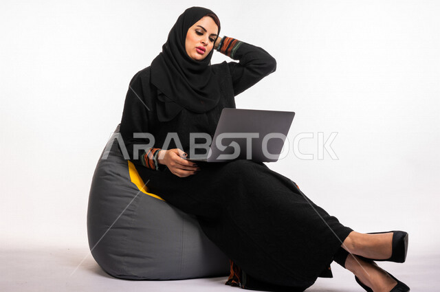  بورتريه لإمرأه عربيه سعوديه خليجيه تجلس على أريكه مريحه, انجاز مهام العمل عبر الحاسوب, إدارة المشاريع عن بعد, اللعب على اللابتوب, إجراء مكالمات فيديو عبر الإنترنت, مشاهدة فلم عبر الجهاز المحمول, تسليه وترفيه, قضاء وقت ممتع