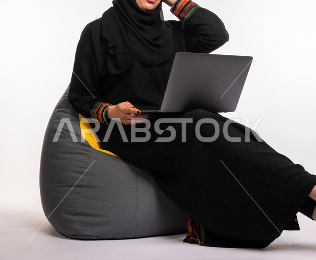  بورتريه لإمرأه عربيه سعوديه خليجيه تجلس على أريكه مريحه, انجاز مهام العمل عبر الحاسوب, إدارة المشاريع عن بعد, اللعب على اللابتوب, إجراء مكالمات فيديو عبر الإنترنت, مشاهدة فلم عبر الجهاز المحمول, تسليه وترفيه, قضاء وقت ممتع