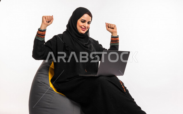 بورتريه لإمرأه عربيه سعوديه خليجيه تجلس على أريكه مريحه, انجاز مهام العمل عبر الحاسوب, إدارة المشاريع عن بعد, اللعب على اللابتوب, إجراء مكالمات فيديو عبر الإنترنت, مشاهدة فلم عبر الجهاز المحمول, تسليه وترفيه, قضاء وقت ممتع