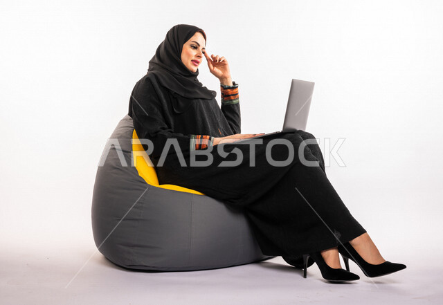  بورتريه لإمرأه عربيه سعوديه خليجيه تجلس على أريكه مريحه, انجاز مهام العمل عبر الحاسوب, إدارة المشاريع عن بعد, اللعب على اللابتوب, إجراء مكالمات فيديو عبر الإنترنت, مشاهدة فلم عبر الجهاز المحمول, تسليه وترفيه, قضاء وقت ممتع