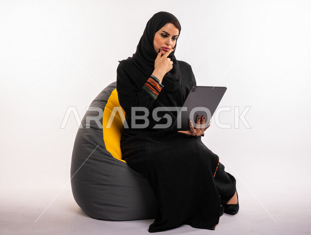 بورتريه لإمرأه عربيه سعوديه خليجيه تجلس على أريكه مريحه, انجاز مهام العمل عبر التابلت, إدارة المشاريع عن بعد, اللعب على الجهاز المحمول, إجراء مكالمات فيديو عبر الإنترنت, مشاهدة فلم, تسليه وترفيه, قضاء وقت ممتع