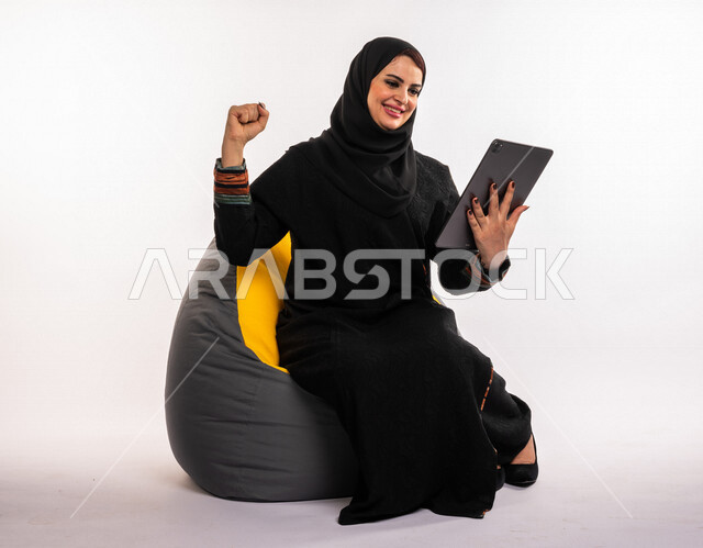 بورتريه لإمرأه عربيه سعوديه خليجيه تجلس على أريكه مريحه, انجاز مهام العمل عبر التابلت, إدارة المشاريع عن بعد, اللعب على الجهاز المحمول, إجراء مكالمات فيديو عبر الإنترنت, مشاهدة فلم, تسليه وترفيه, قضاء وقت ممتع