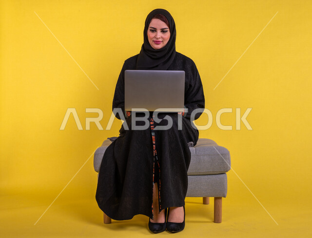 بورتريه لسيدة عربية خليجية سعودية تستخدم الحاسوب المحمول لانجاز الاعمال عن بعد ، اجراء مكالمات الفيديو ، مشاهدة البرامج والافلام ،  التسويق الالكتروني ، تصفح الانترنت ،  خلفية صفراء