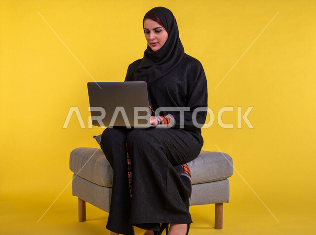 بورتريه لسيدة عربية خليجية سعودية تستخدم الحاسوب المحمول لانجاز الاعمال عن بعد ، اجراء مكالمات الفيديو ، مشاهدة البرامج والافلام ،  التسويق الالكتروني ، تصفح الانترنت ،  خلفية صفراء