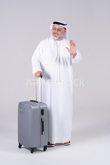 رجل إماراتي مسن مع حقيبة سفر يلوح بيده