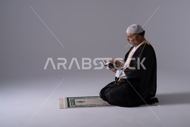 Emirati Man Reading Quran on Prayer Rug in Studio
