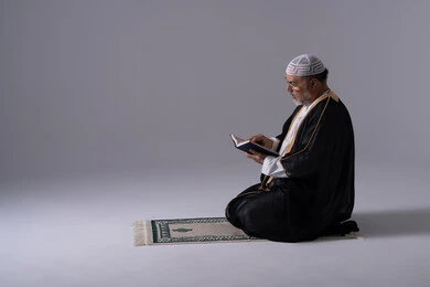 Emirati Man Reading Quran on Prayer Rug in Studio