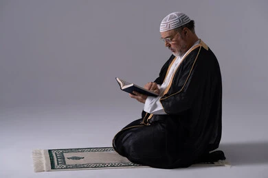 رجل إماراتي بالبشت يقرأ القرآن على سجادة الصلاة