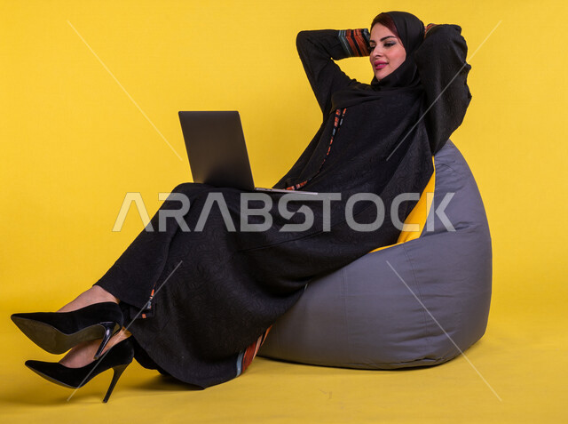 بورتريه لسيدة عربية خليجية سعودية تستخدم الحاسوب المحمول لانجاز الاعمال عن بعد ، اجراء مكالمات الفيديو ، مشاهدة البرامج والافلام ،  التسويق الالكتروني ، تصفح الانترنت ،  خلفية صفراء