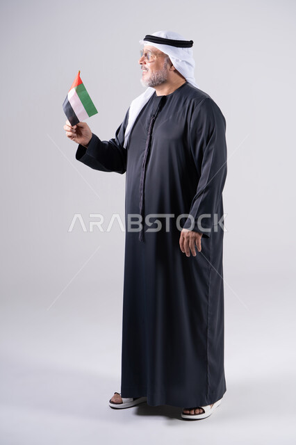 رجل إماراتي بالزي التقليدي يحمل علم الإمارات