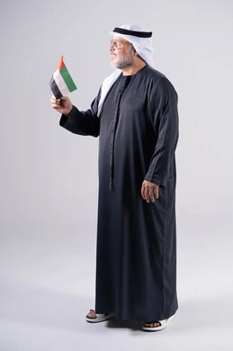 رجل إماراتي بالزي التقليدي يحمل علم الإمارات