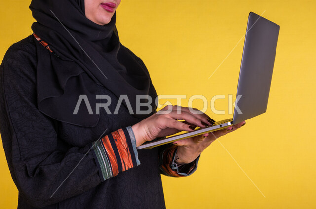 بورتريه لسيدة عربية خليجية سعودية تستخدم الحاسوب المحمول لانجاز الاعمال عن بعد ، اجراء مكالمات الفيديو ، مشاهدة البرامج والافلام ،  التسويق الالكتروني ، تصفح الانترنت ،  خلفية صفراء