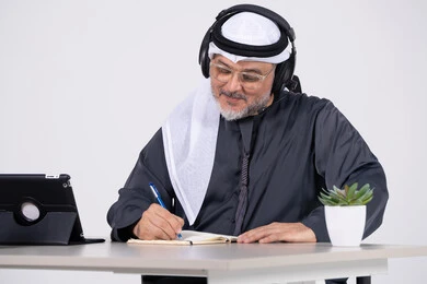رجل إماراتي يرتدي سماعات ويكتب على المكتب